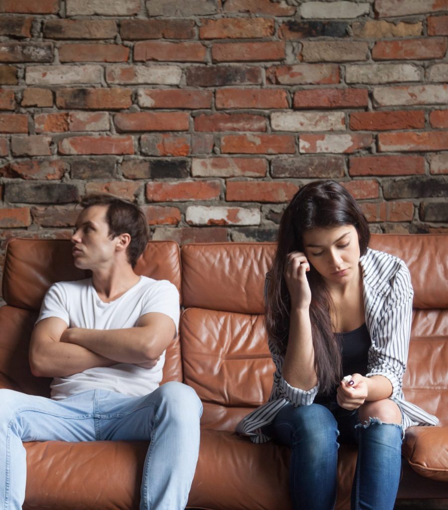 Frustrated upset couple in quarrel not talking after fight, offended stubborn insulted jealous man sitting silent on sofa at home with sad depressed disappointed woman, marriage relationships problem